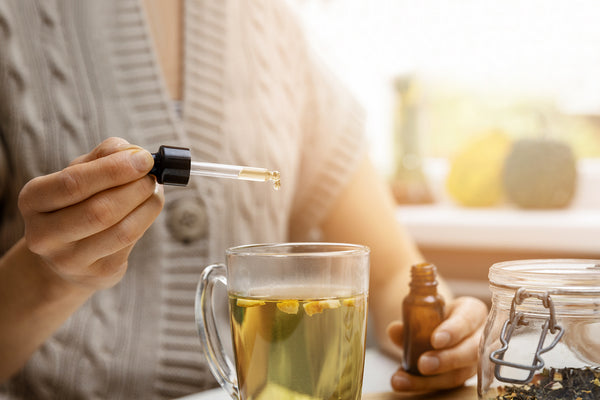 women in sweater dropping cbd oil drops by pipette into her teacup
