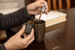 Individual using a dropper to squeeze Infused Amphora CBD oil drops into their drink