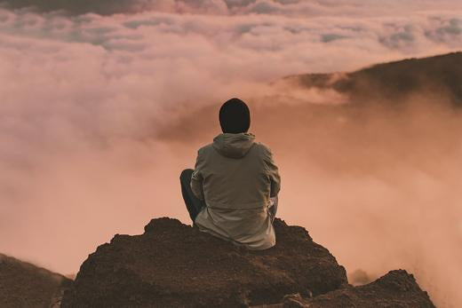 A man sitting above the clouds on a mountain, meditating, experiencing pain and stress relief from CBD  