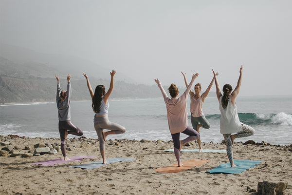 4 women and an instructor practicing yoga and healthy living on a UK beach
