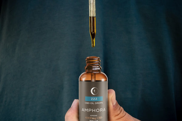 hand holding bottle of Infused Amphora ZZZ CBD oil drops while pulling out the dropper