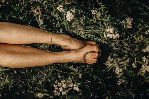 A woman lying in a field of grass with her feet enveloped by the grass blades, experiencing the wellness effect of CBD 