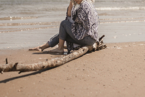 A woman sitting on a log on a beach, calmly experiencing the wellness effect of CBD 
