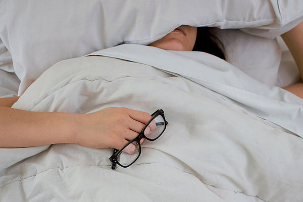 Individual in bed under white sheets and with head under the pillow. Sleeping well with ZZZ CBD oil uk