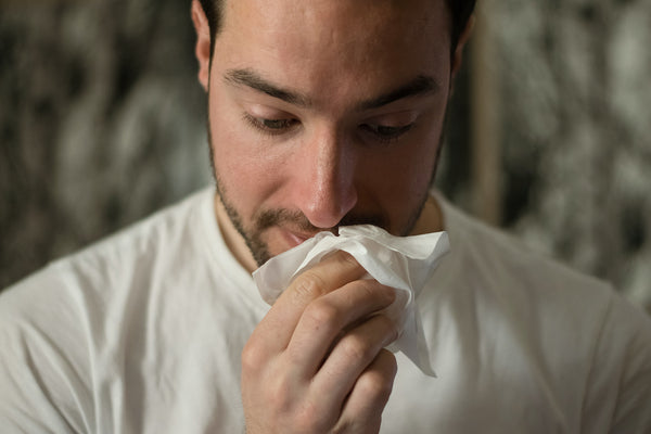 A man holding a tissue below his nose. Incorporate CBD to help remedy cold  